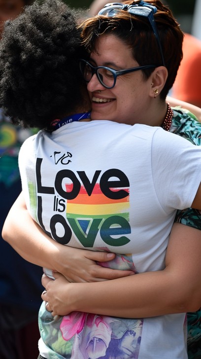 Imagen de dos personas abrazadas, mientras una de ellas tiene una playera con la leyenda: “amor es amor”, lo que simboliza disfrutar del amor consciente.