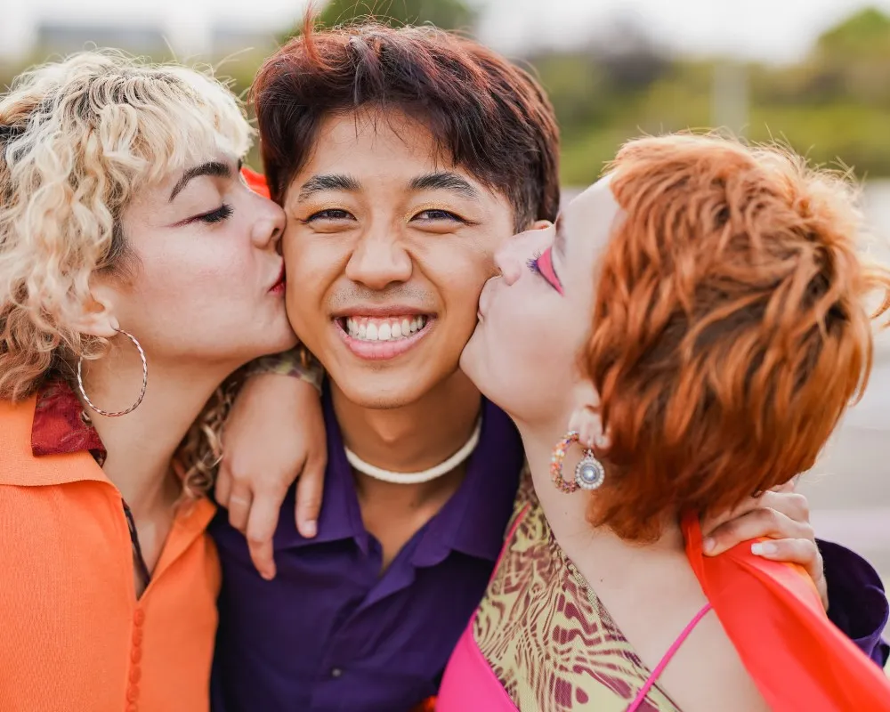 :¿cómo saber si el amor libre es para mí?, tres personas en el exterior, felices, le dan un beso en la mejilla a la persona de en medio